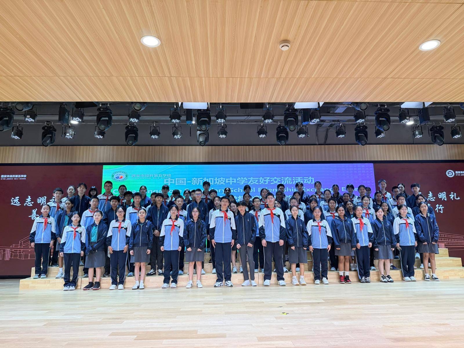 Large group of students in school uniforms posing on a stage at a China-Singapore secondary school friendship exchange event.