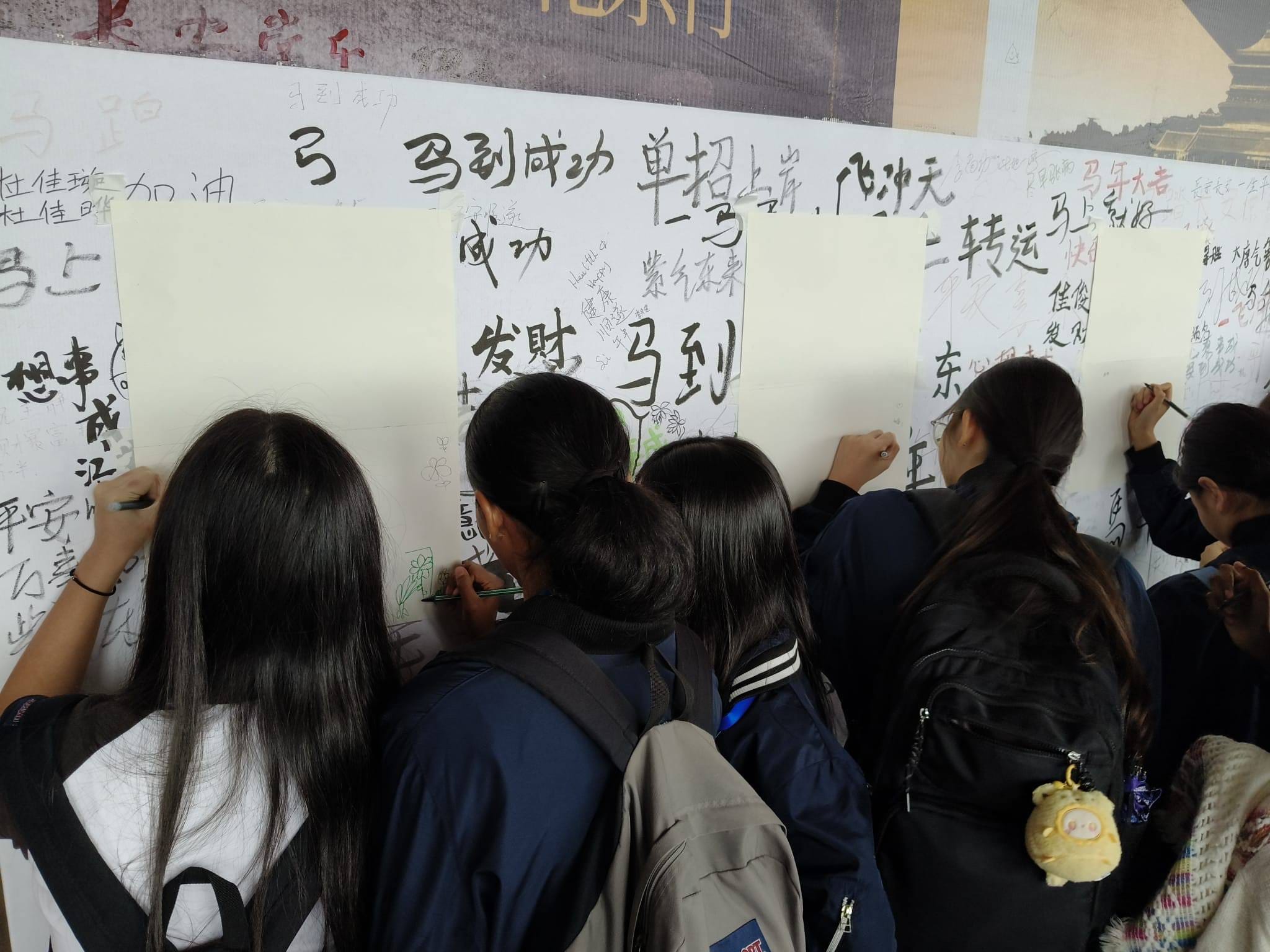 Several young people with dark hair write Chinese characters on large white boards mounted on a wall.