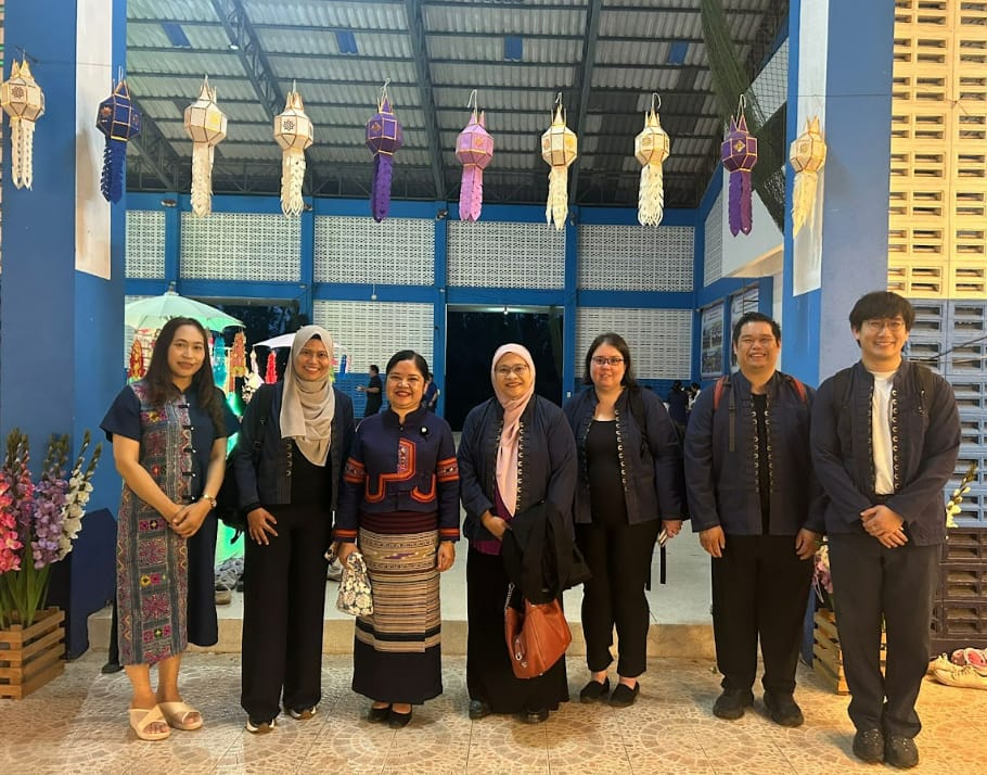 Seven people pose together under hanging decorative lanterns outside a blue building at a cultural event.