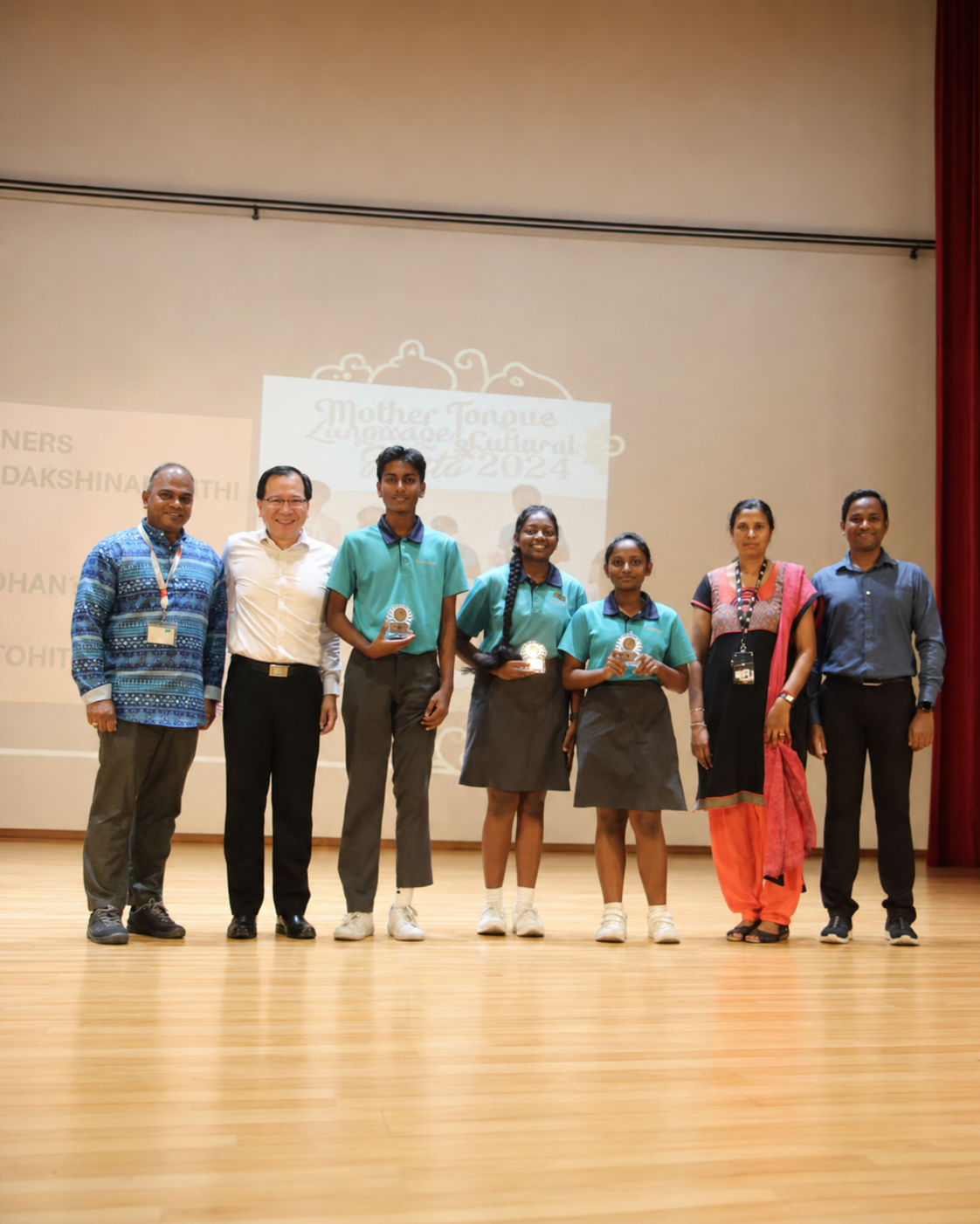 3 students and 4 adults pose on stage with prizes
