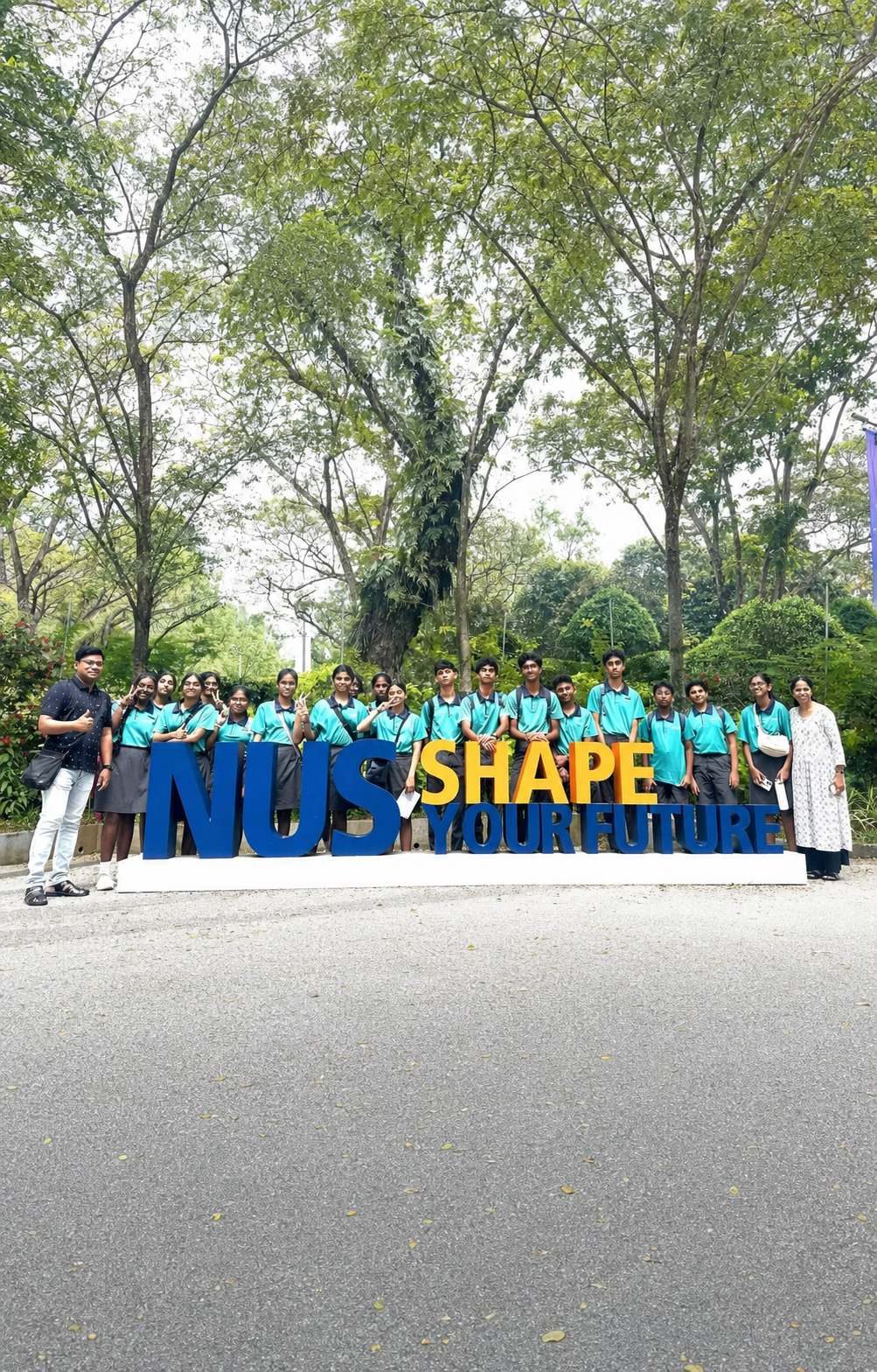 Group of students in teal uniforms posing behind large NUS Shape Your Future letters outdoors.