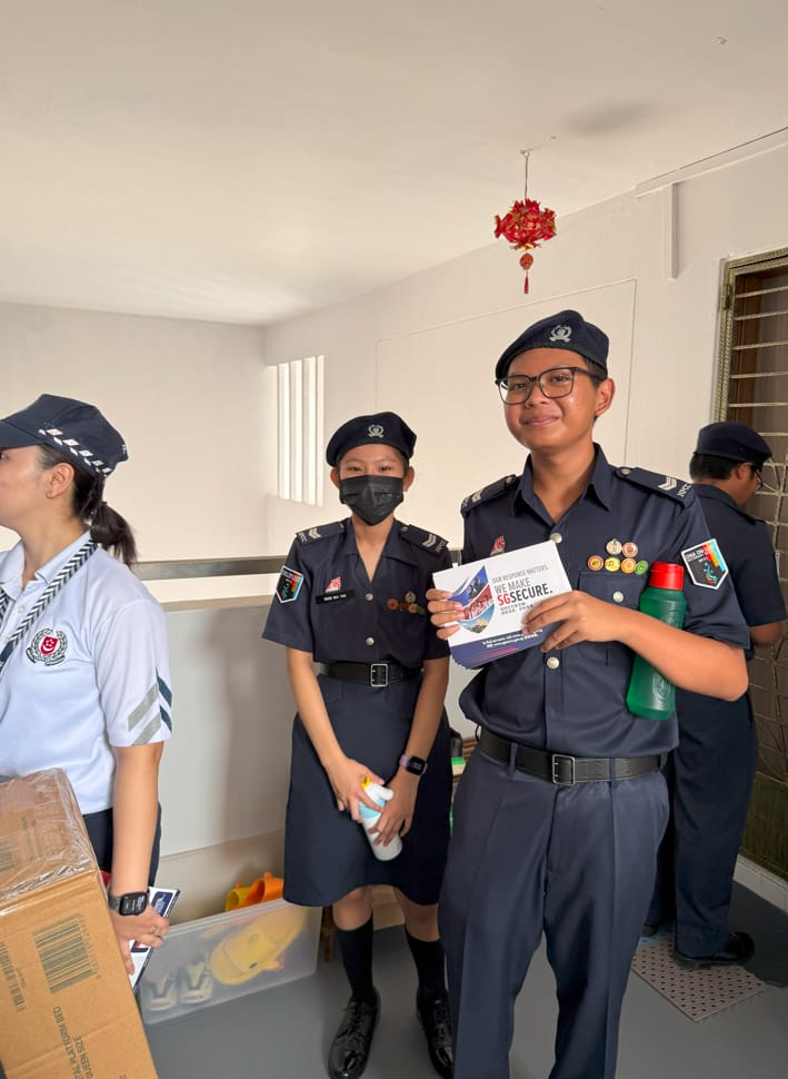 Four uniformed officers in dark navy uniforms inside a room, one holding a SGSecure pamphlet and smiling.