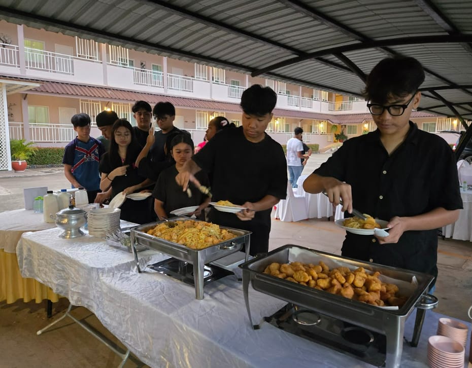 Teenagers in black clothing serve themselves from buffet trays of fried food at an outdoor event near a building.