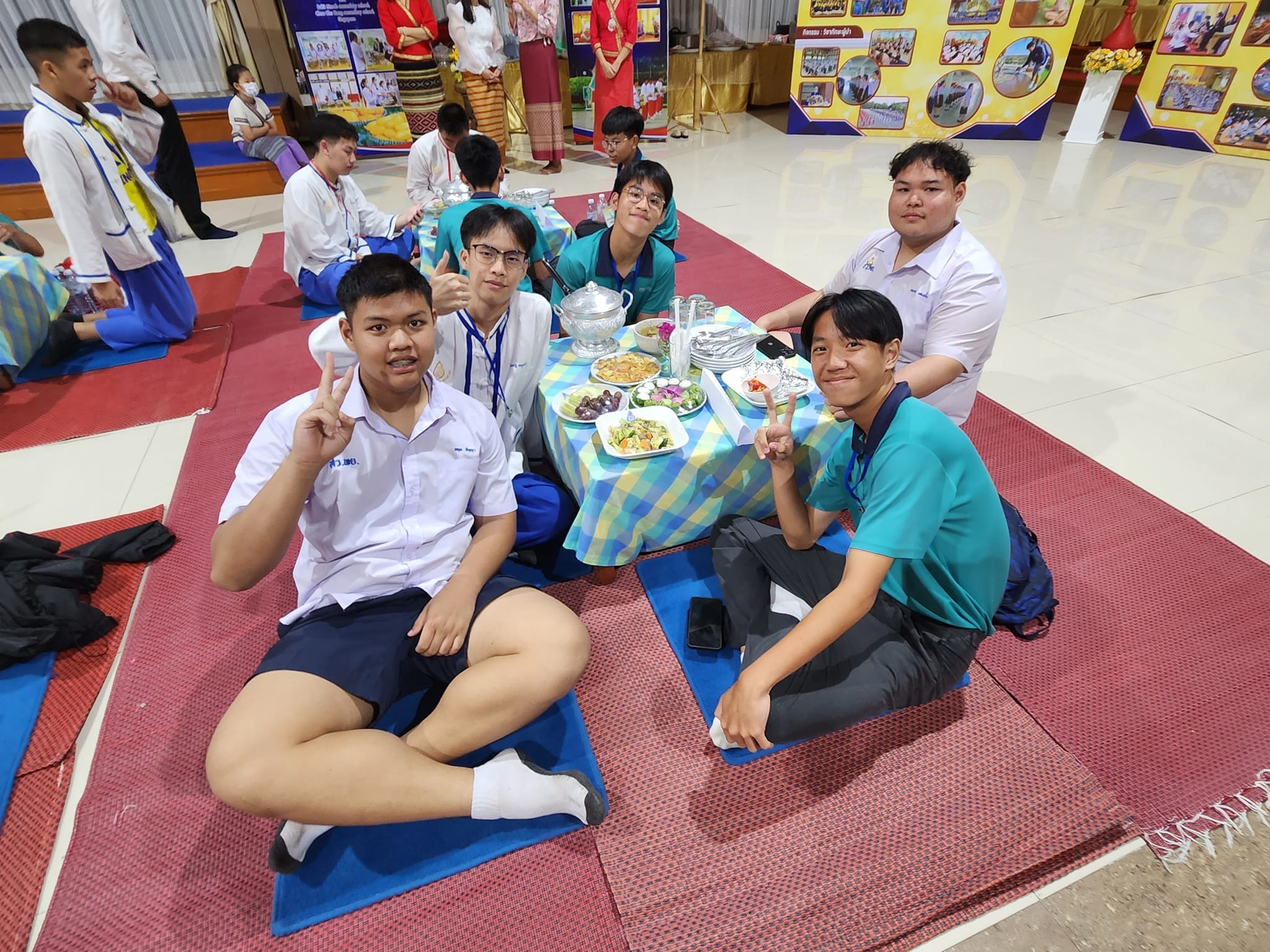 Students and teachers sitting on the floor for a meal.