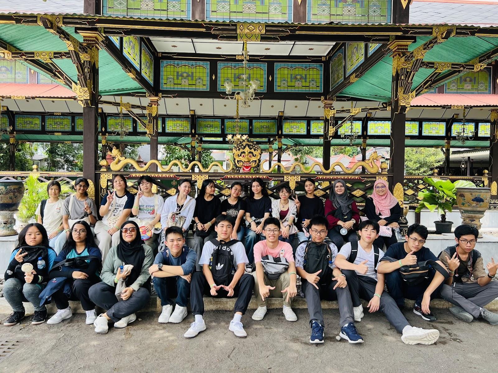 A large group of young people posing in front of an ornate traditional Javanese pavilion with gold and green decor.