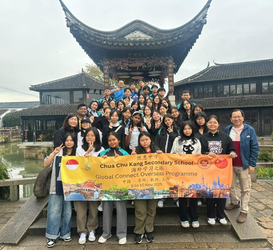 A large student group holds a Chua Chu Kang Secondary School Global Connect Overseas Programme banner in front of a Chinese pavilion.