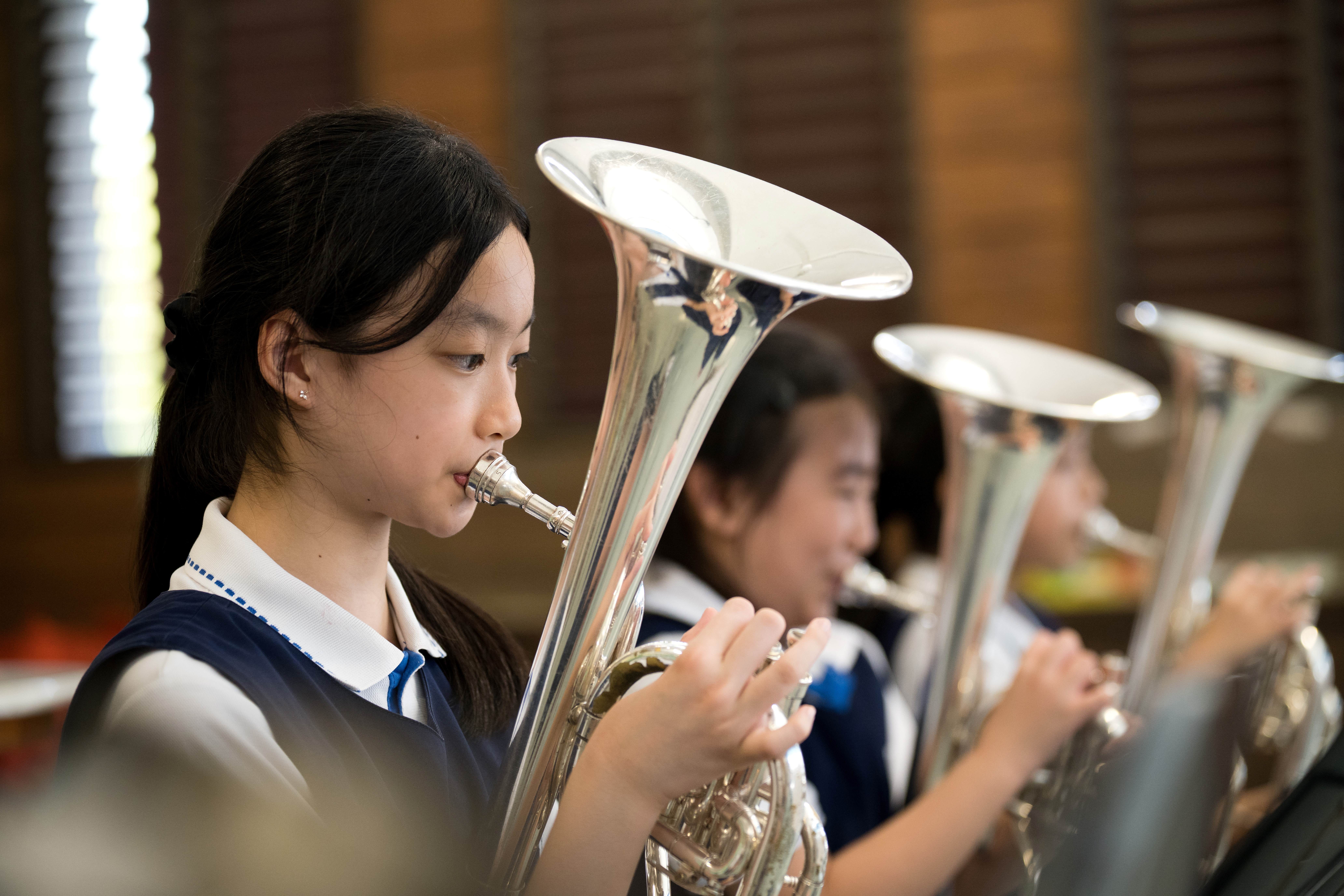 Student in uniform plays a silver tuba in band practice, with other tuba players blurred behind.