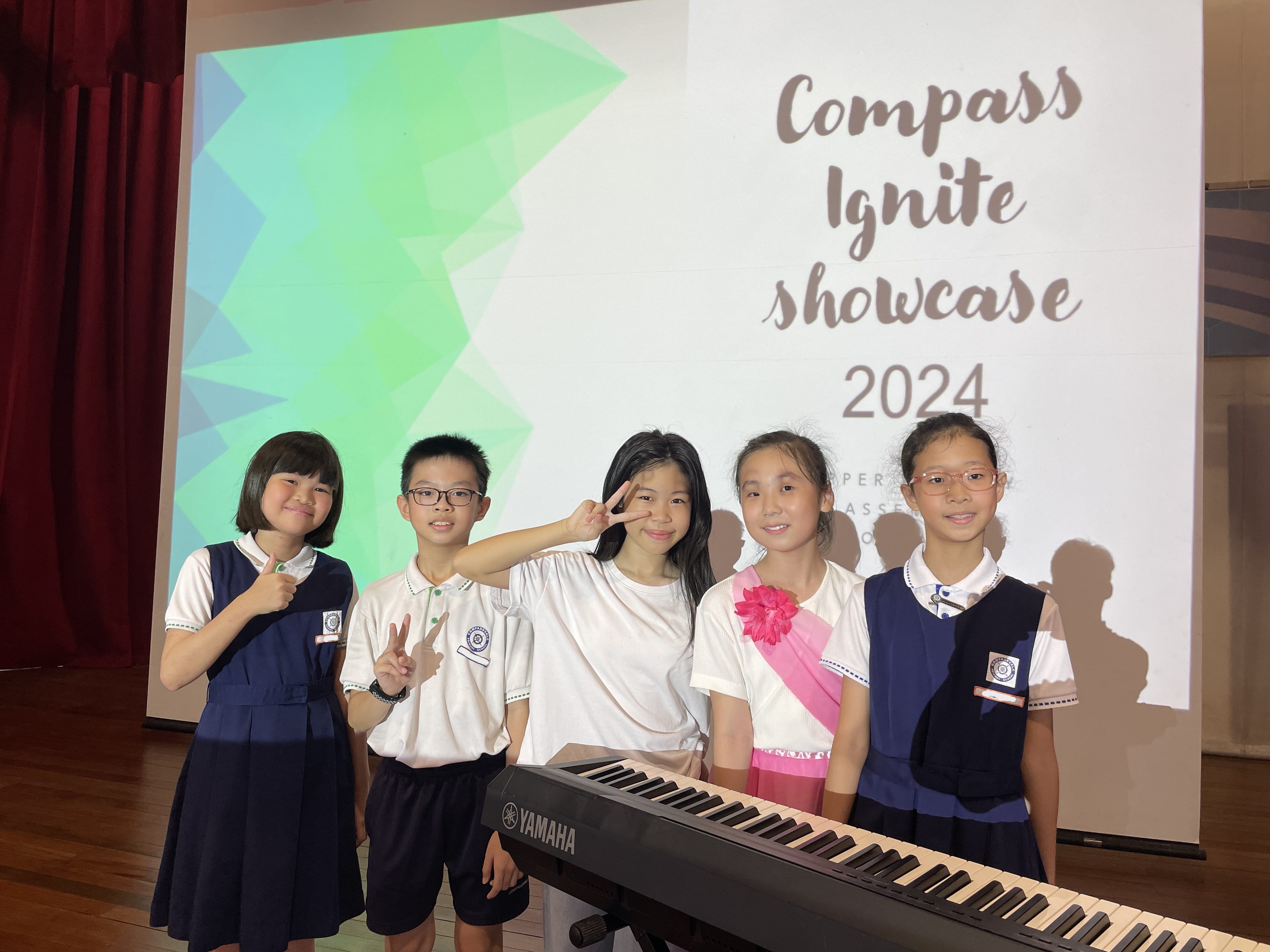Five children in school uniforms pose by a Yamaha keyboard before a Compass Ignite Showcase 2024 screen.