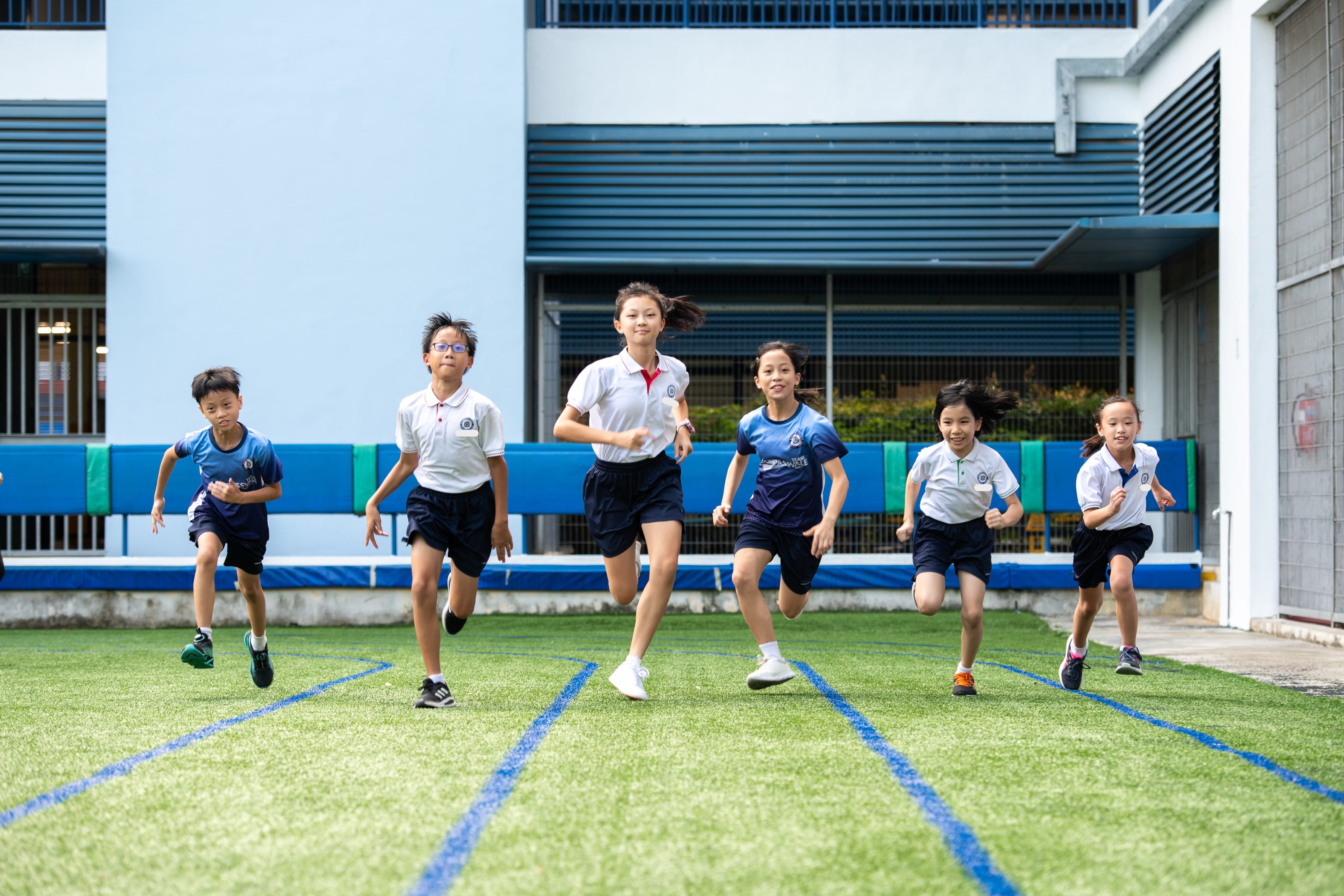 Six children in school uniforms running toward the camera on a green artificial turf field.