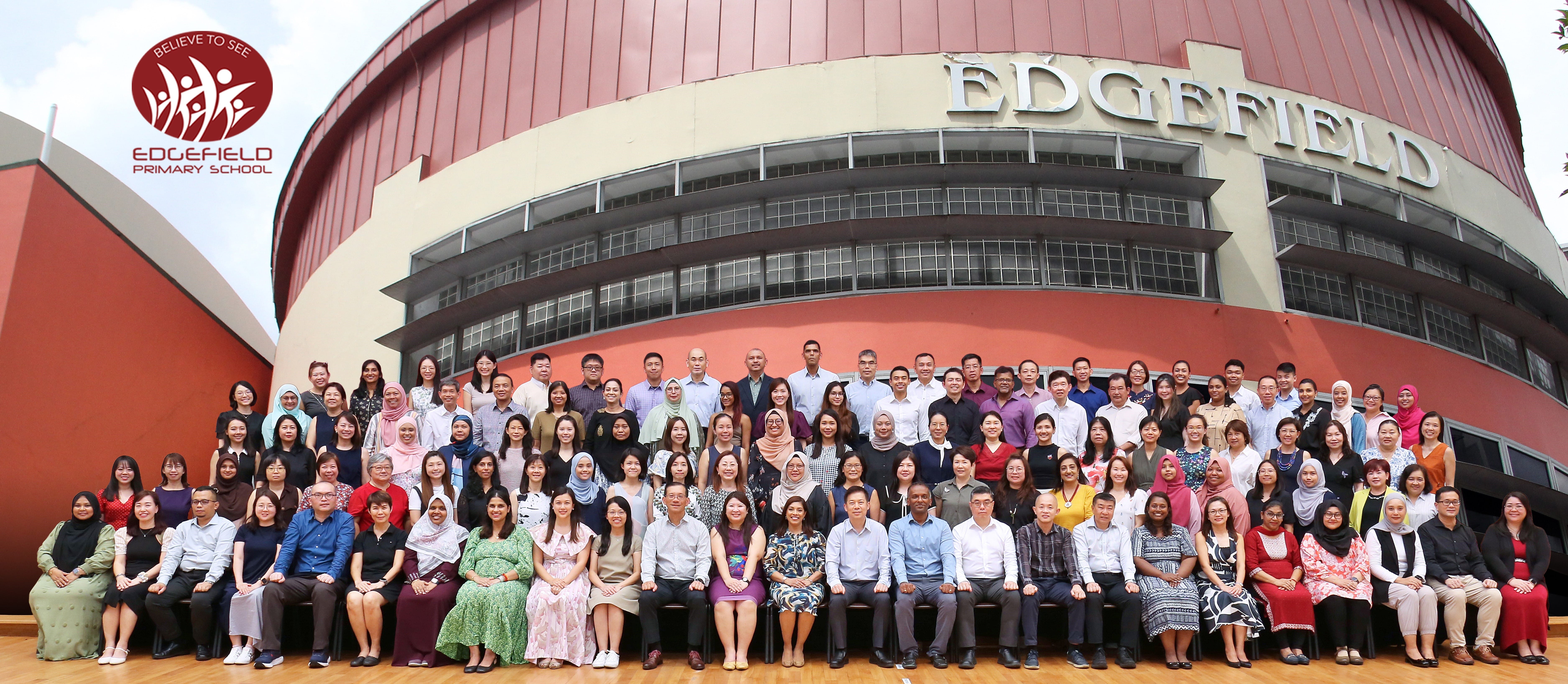 Large group photo of staff seated and standing outside Edgefield Primary School building.