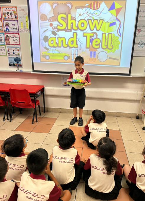 A student holds a colorful toy while presenting at a Show and Tell session to seated classmates at Edgefield Primary.