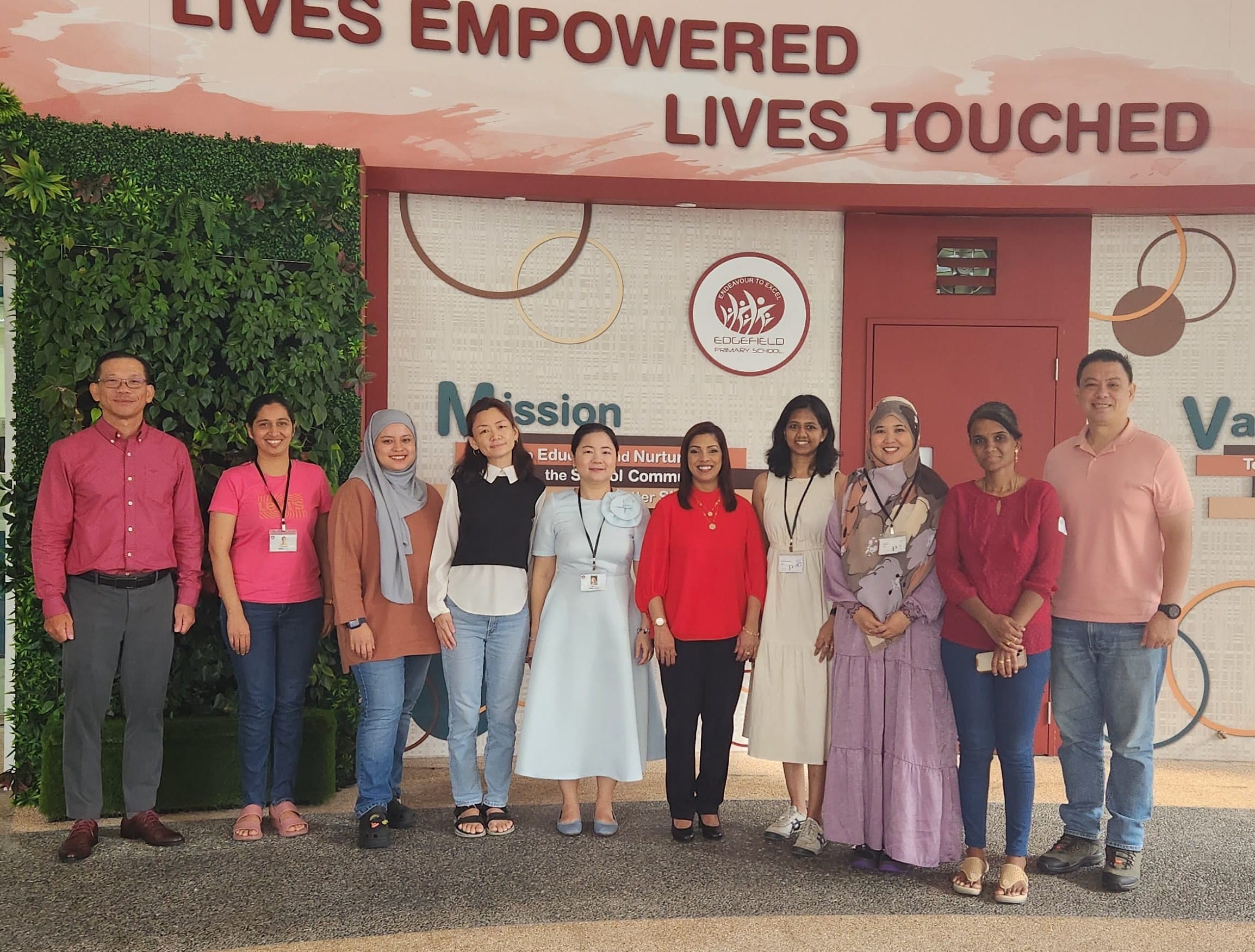 Ten adults posing in front of Edgefield Primary School's wall reading "Lives Empowered Lives Touched."