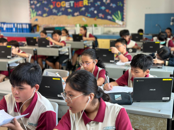 Students in maroon uniforms work on ASUS laptops in a colorful classroom with a "Together" bulletin board.