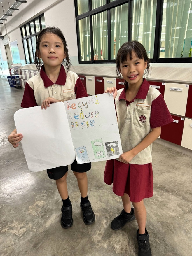 Two young schoolgirls in uniforms holding a handmade poster reading Recycle, Reduce, Reuse with colorful drawings.