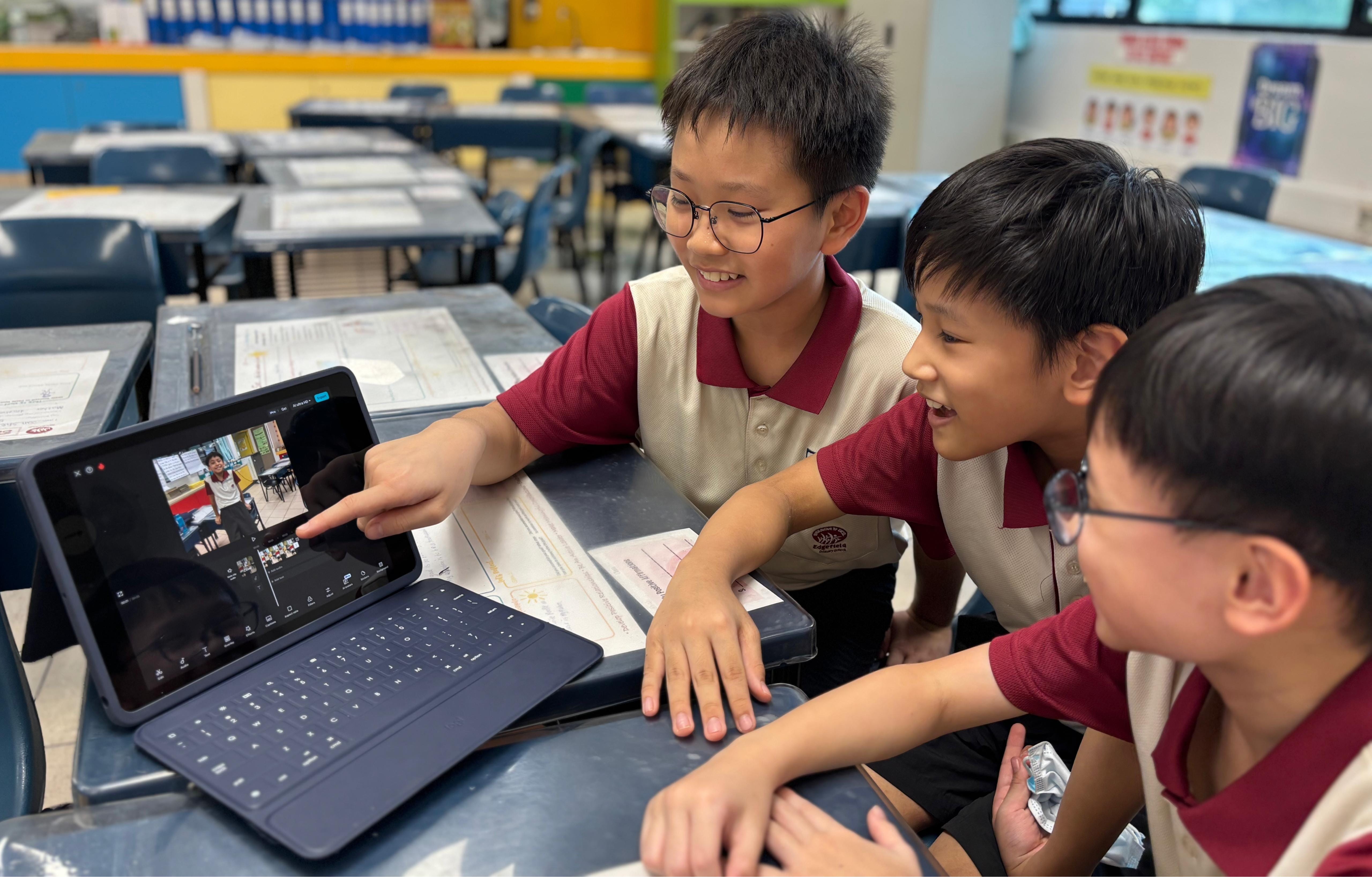 Three boys in school uniforms gather around a tablet with a keyboard, smiling as one points at the screen.
