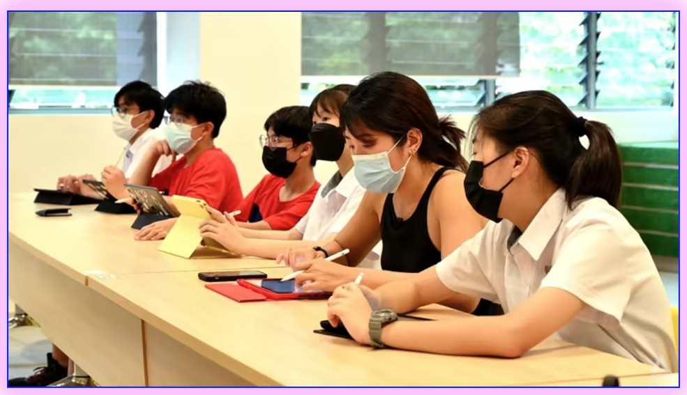 Six students wearing face masks sit at a long desk using tablets in a classroom.