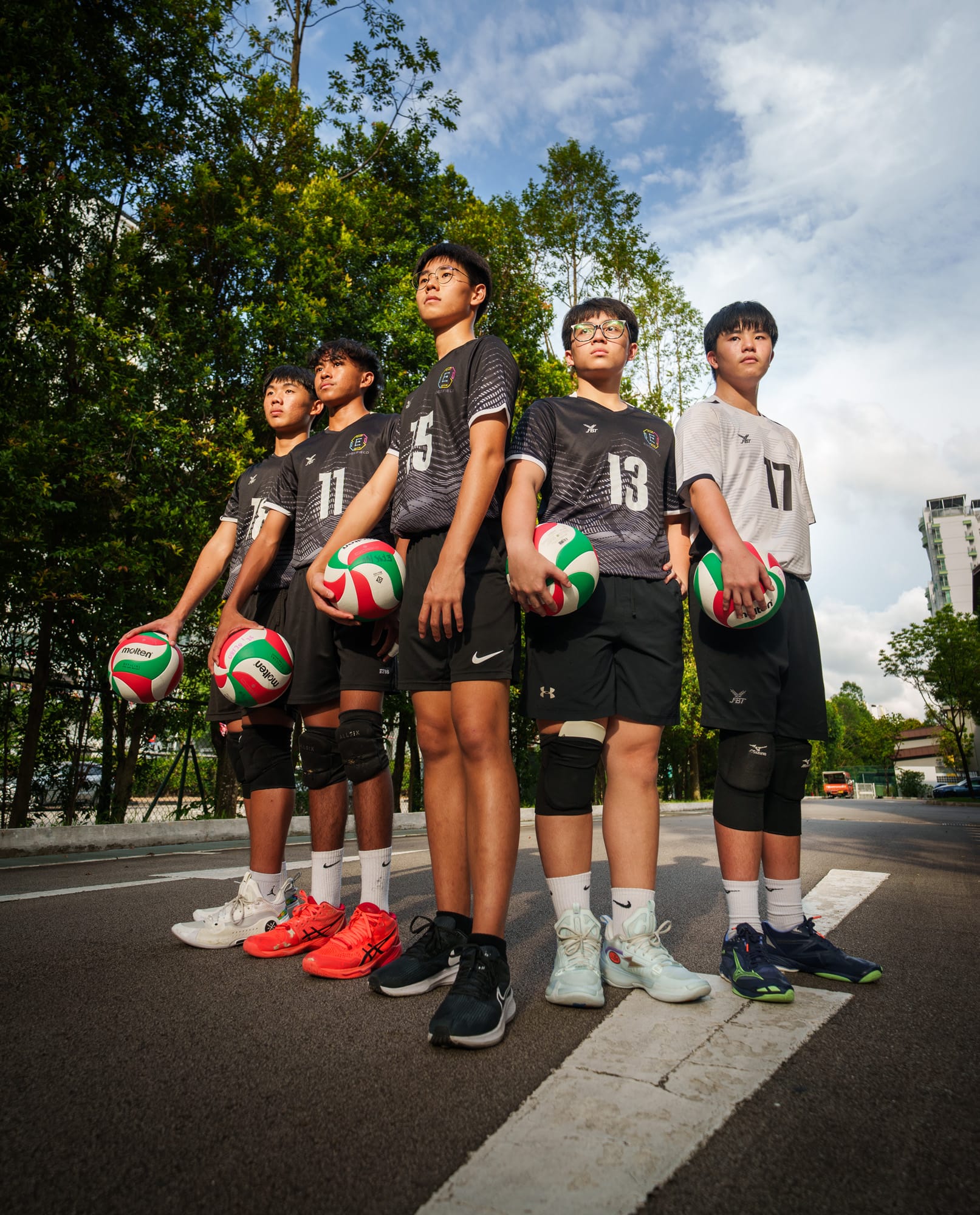 Five young volleyball players in numbered jerseys hold Molten balls while standing outdoors on a court.