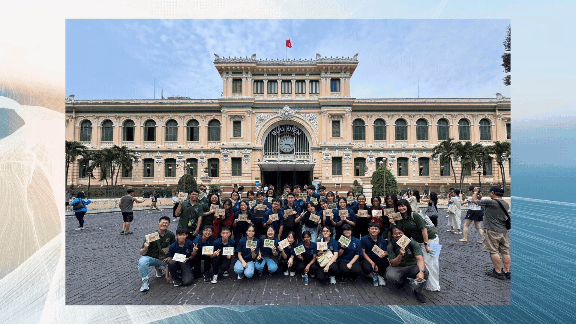 A large group of students in blue uniforms pose holding cards in front of the Buu Dien post office in Ho Chi Minh City.