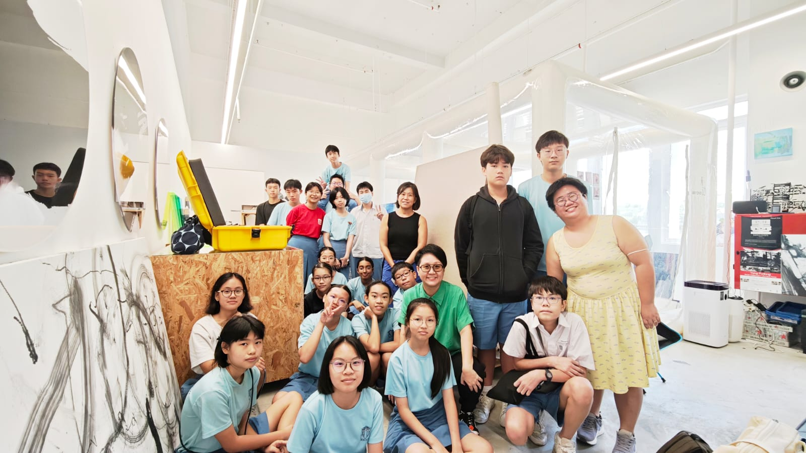 A large group of young students and adults posing together inside a bright white art studio.