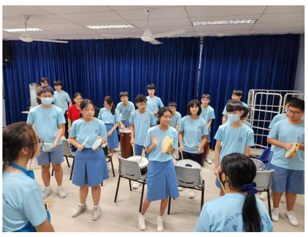 Students in matching blue uniforms play various percussion instruments in a room with blue curtains.
