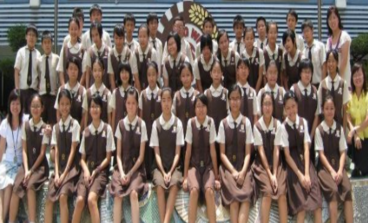 Large group of students in brown and white school uniforms posing in rows outdoors for a group photo.