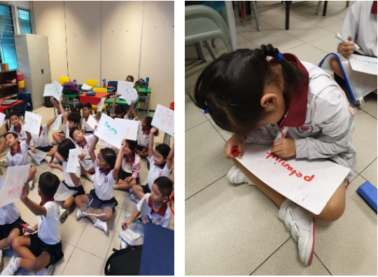 Young children in uniforms sit on a classroom floor holding up paper signs with red writing.