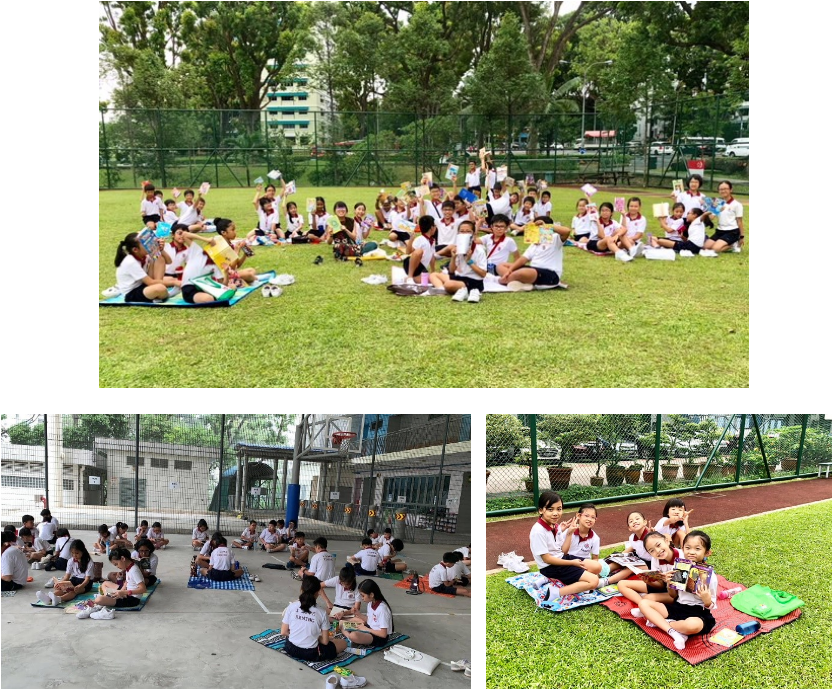 Children in school uniforms sit outdoors on mats holding up books on a grass field and courtyard.