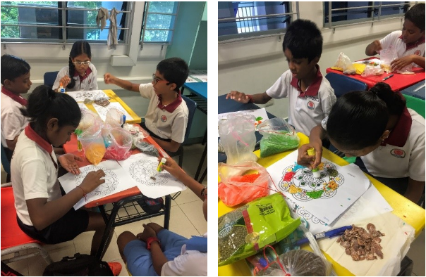 Children in school uniforms sit at desks doing a craft activity with colorful materials and printed sheets.