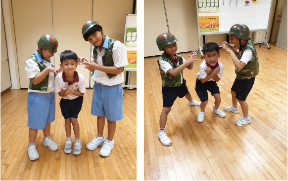 Three young children wearing green military helmets and camouflage vests pose playfully on a wooden floor indoors.