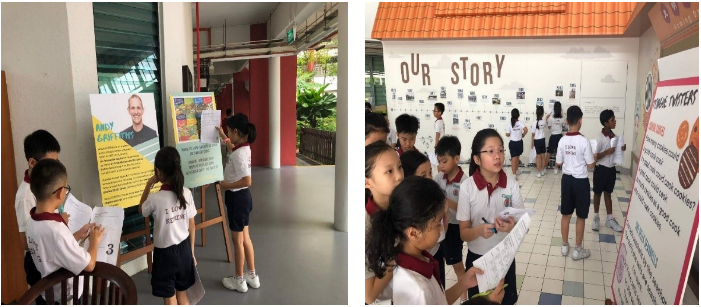 Students in school uniforms viewing and writing notes at educational display boards and an "Our Story" wall exhibit.