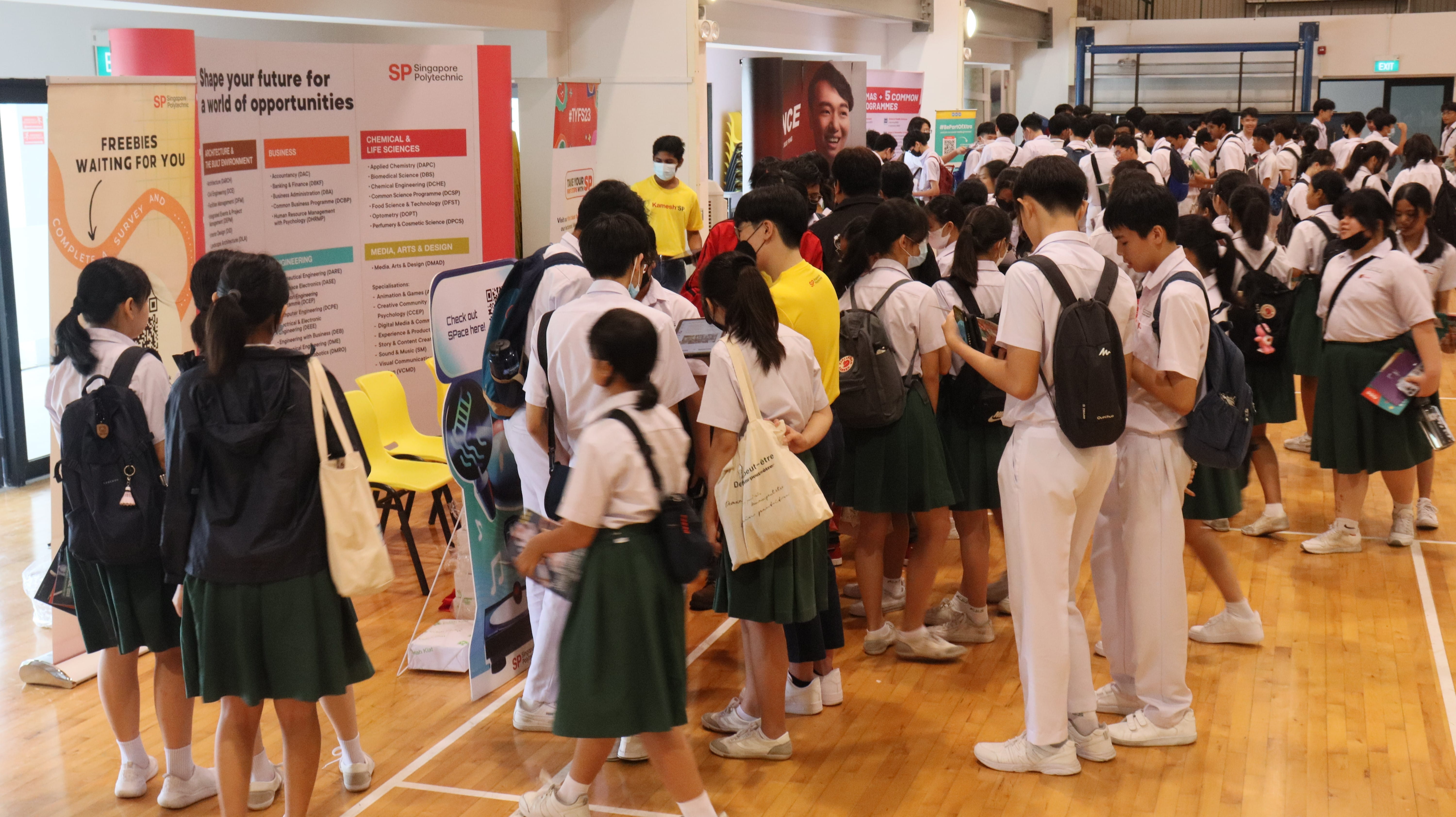Students in school uniforms gather around Singapore Polytechnic promotional banners at an indoor education fair.