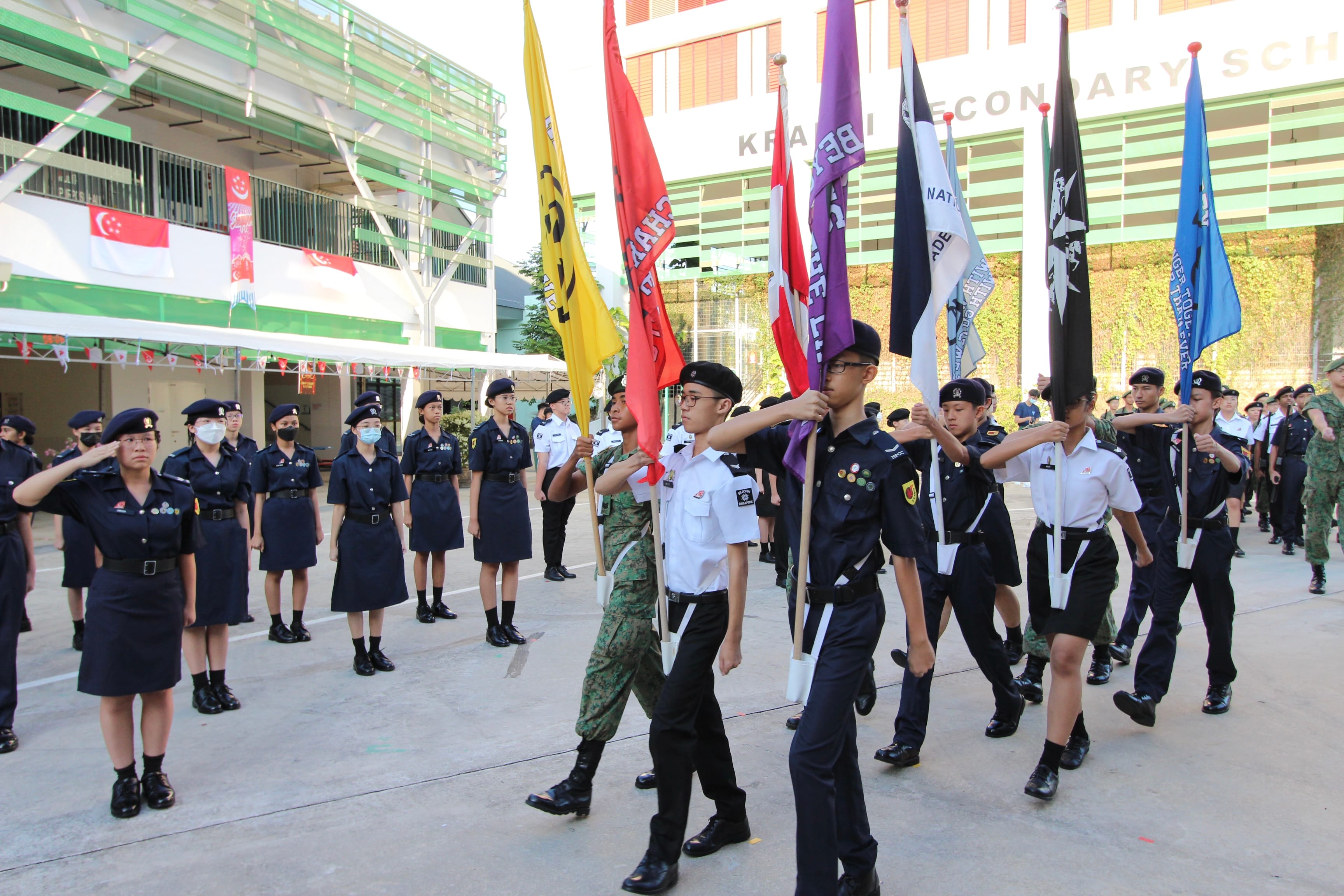 Students in uniform march carrying colorful flags during a parade at Kranji Secondary School.