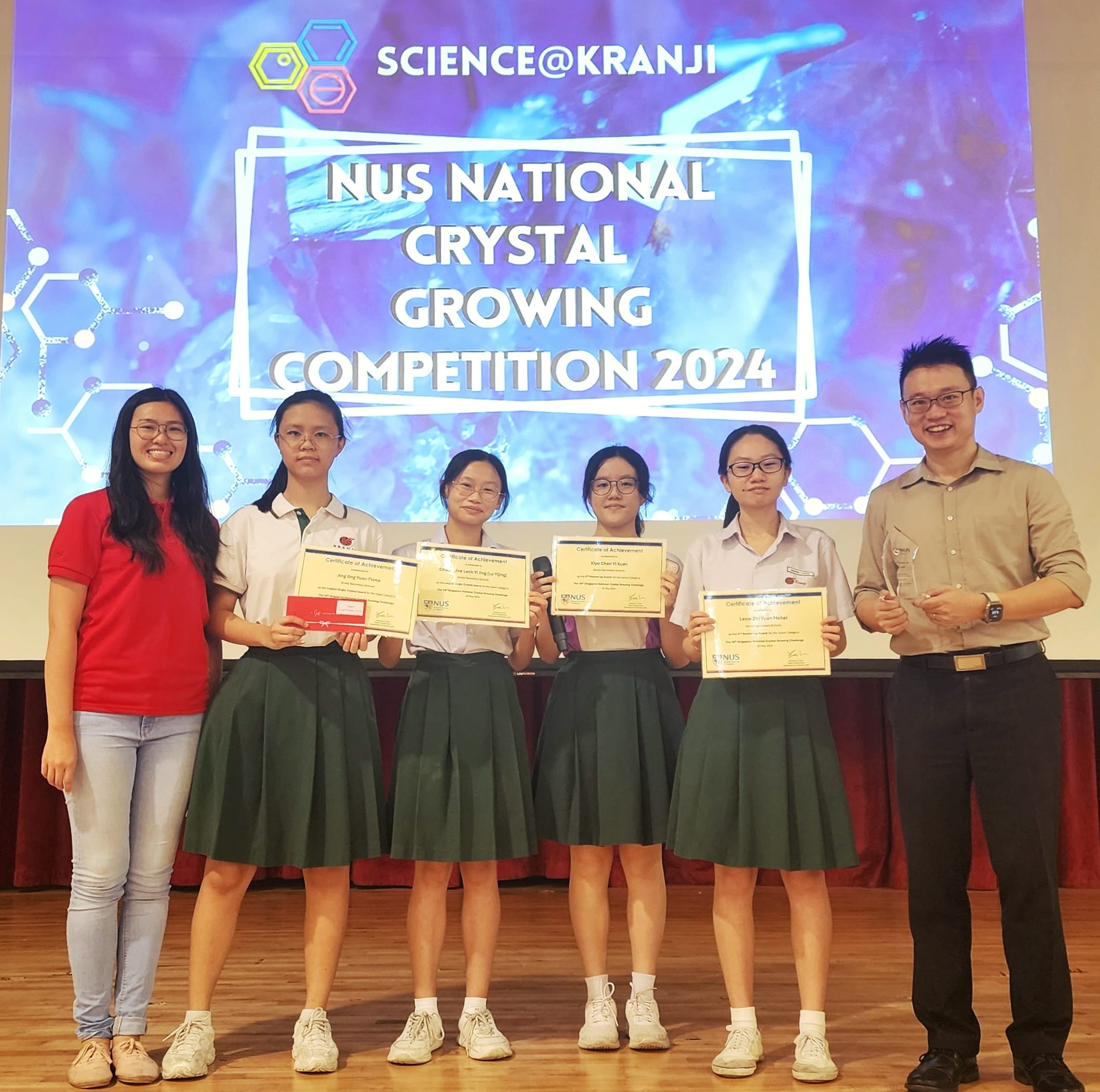 Six people pose on a stage holding certificates at the NUS National Crystal Growing Competition 2024.
