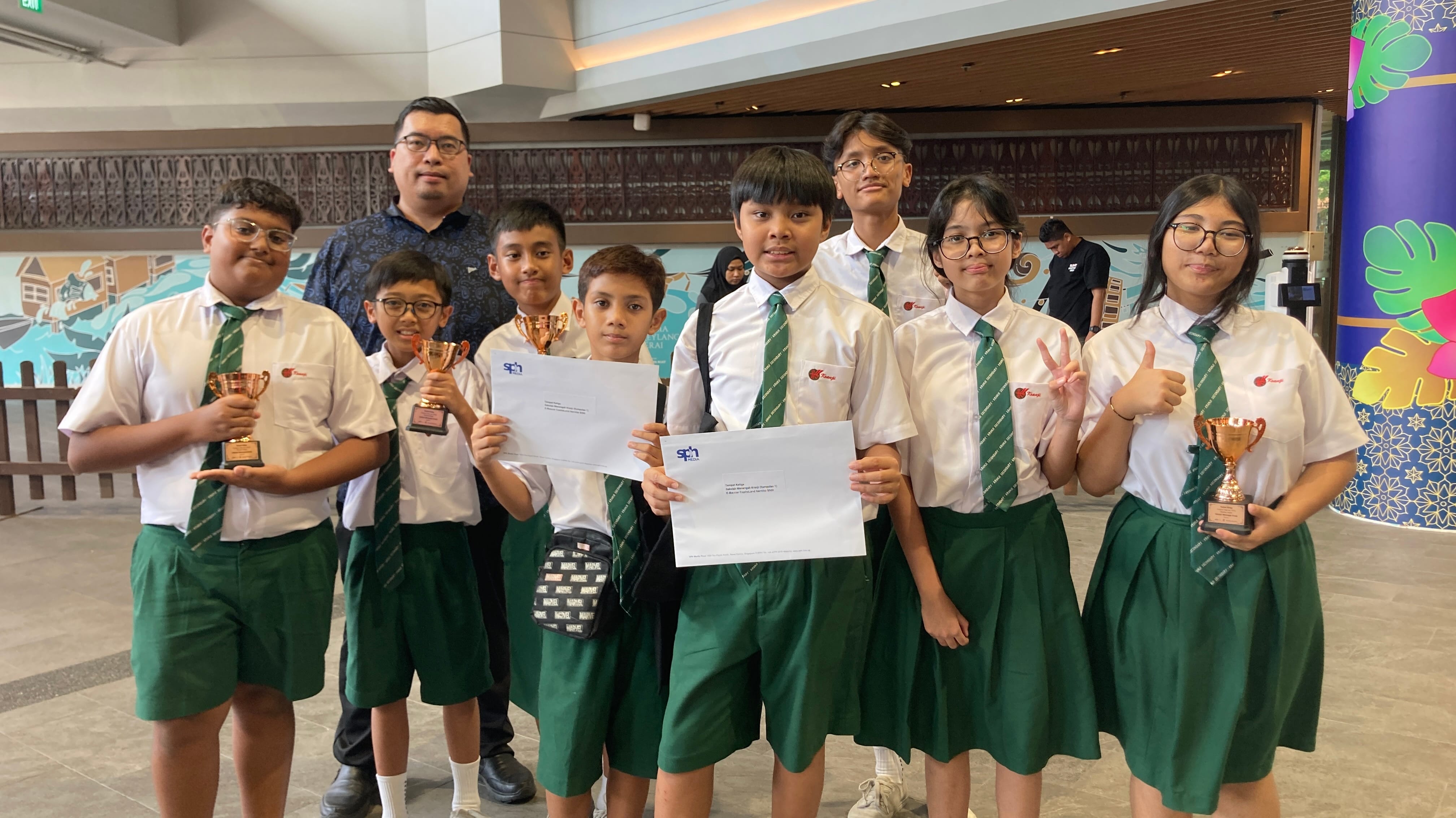 Group of school students in white shirts and green ties holding trophies and certificates, posing with an adult.