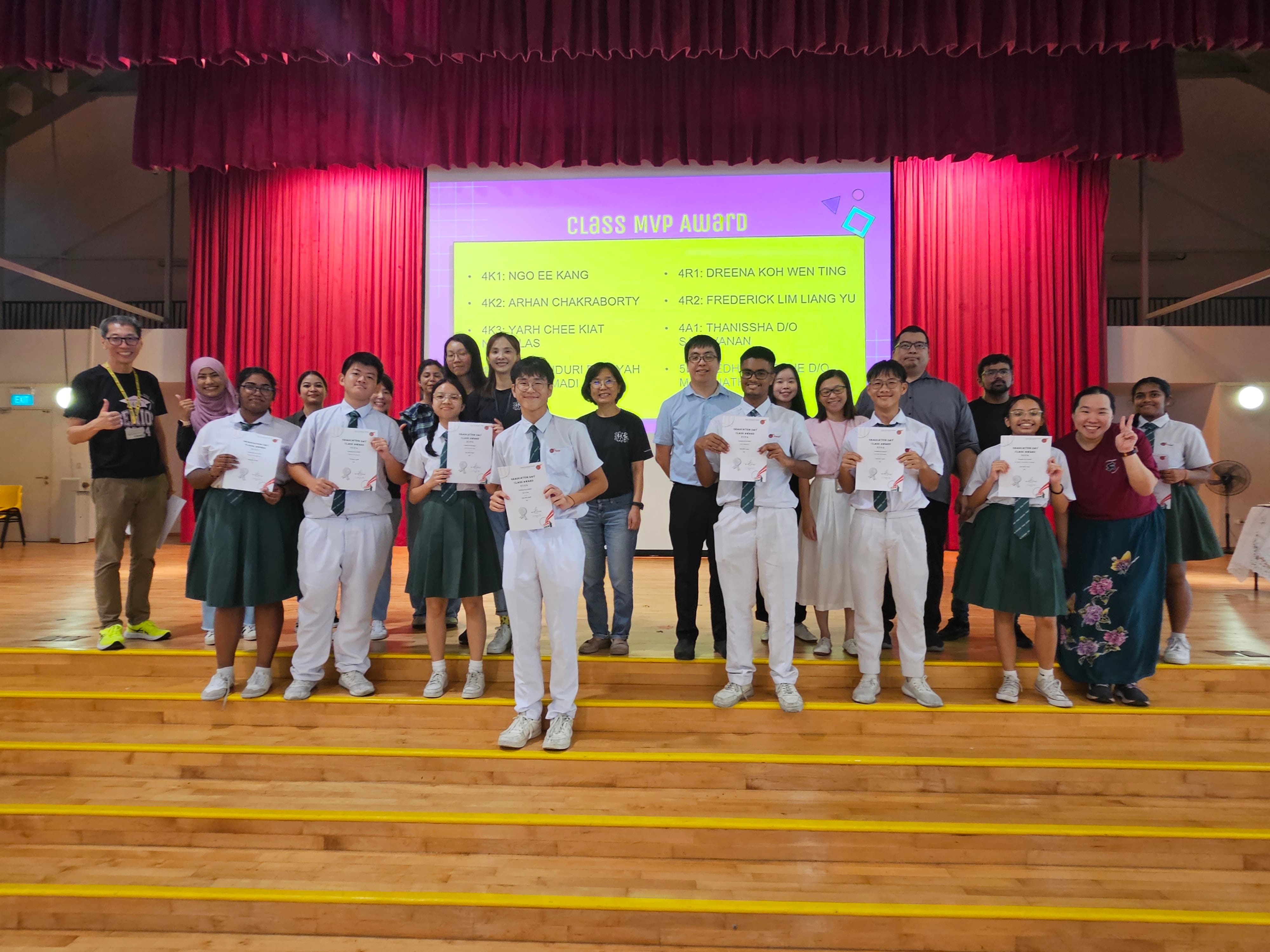 Students and teachers pose on stage holding certificates in front of a Class MVP Award presentation screen.