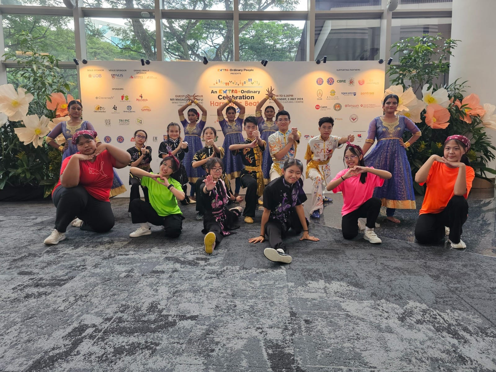 A large group of youth in cultural and casual costumes pose in front of an Extra-Ordinary Celebration event banner.