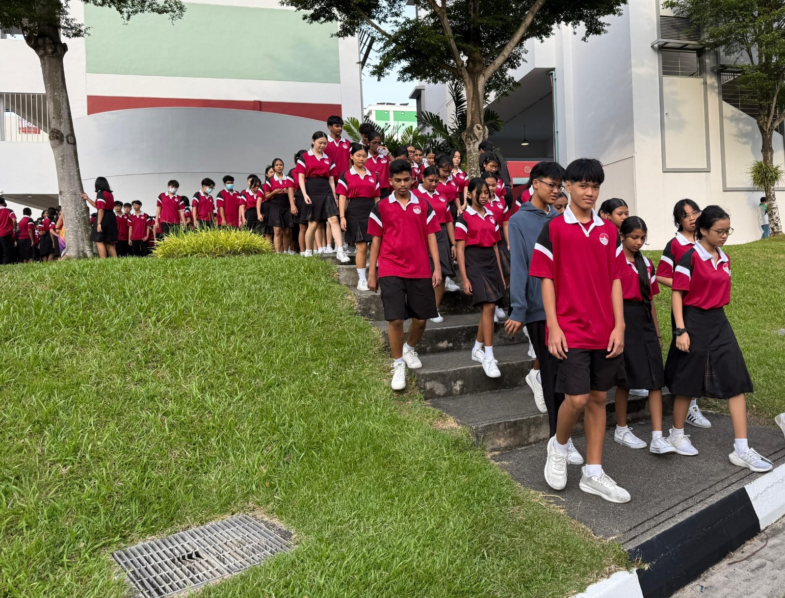 Students in red and black school uniforms walk down outdoor steps beside a white school building.