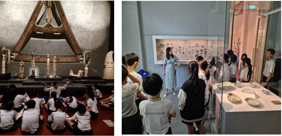 Students in white uniforms on a museum field trip, sitting before wooden artifacts and viewing ceramic exhibits with a guide.