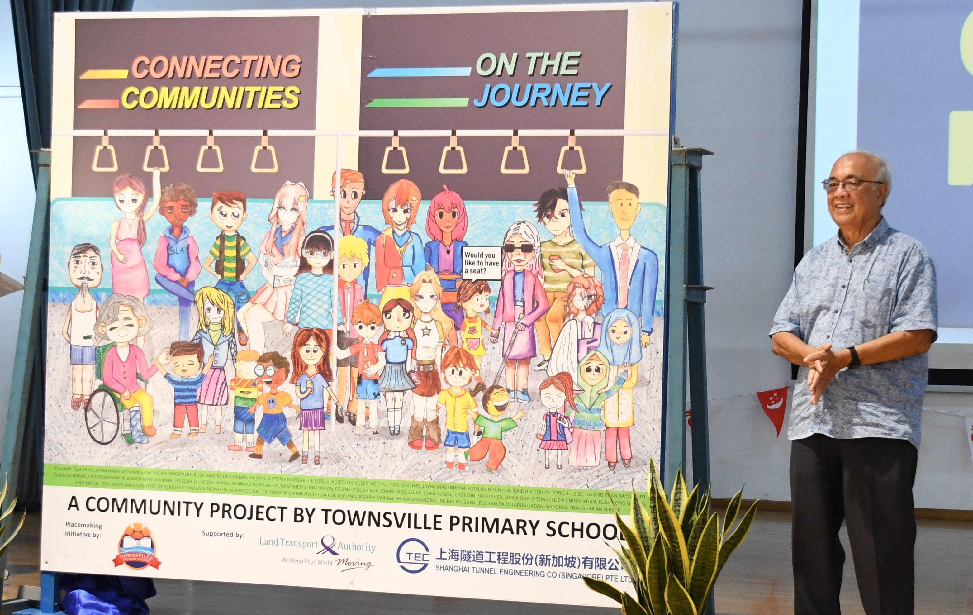 Man stands beside poster reading Connecting Communities On the Journey, with colorful drawn passengers on a train.