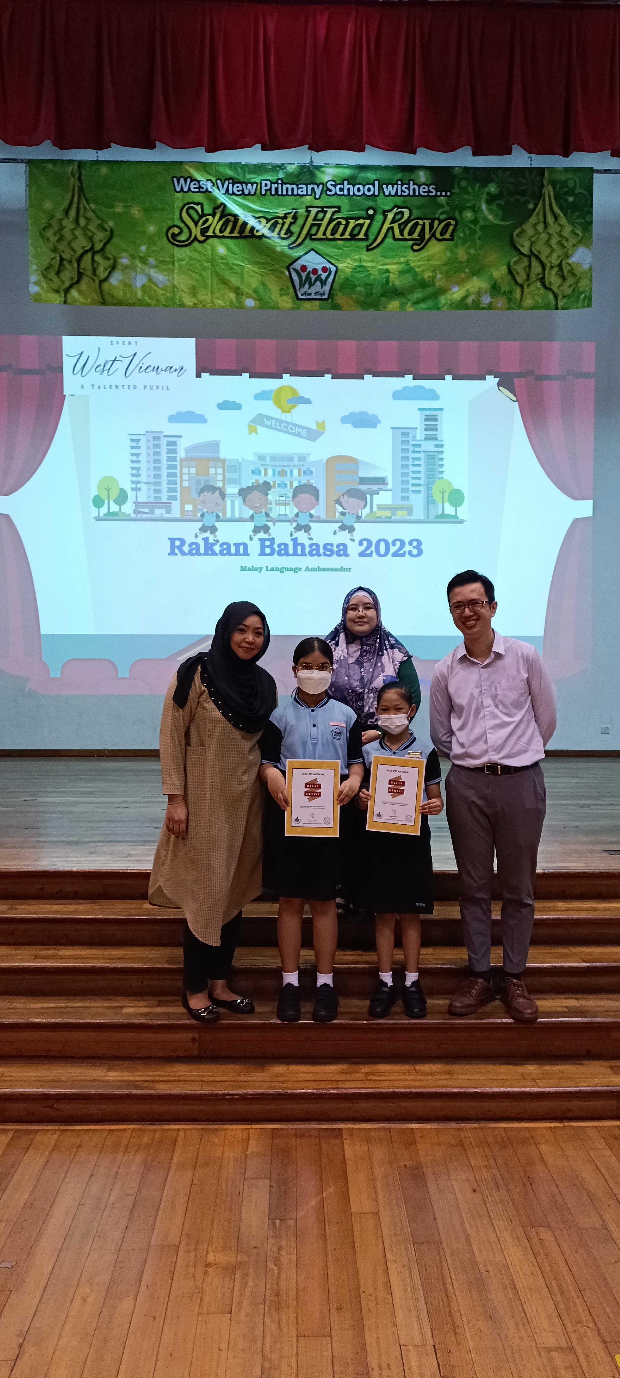 Two students holding certificates pose with three adults at West View Primary School's Rakan Bahasa 2023 event.