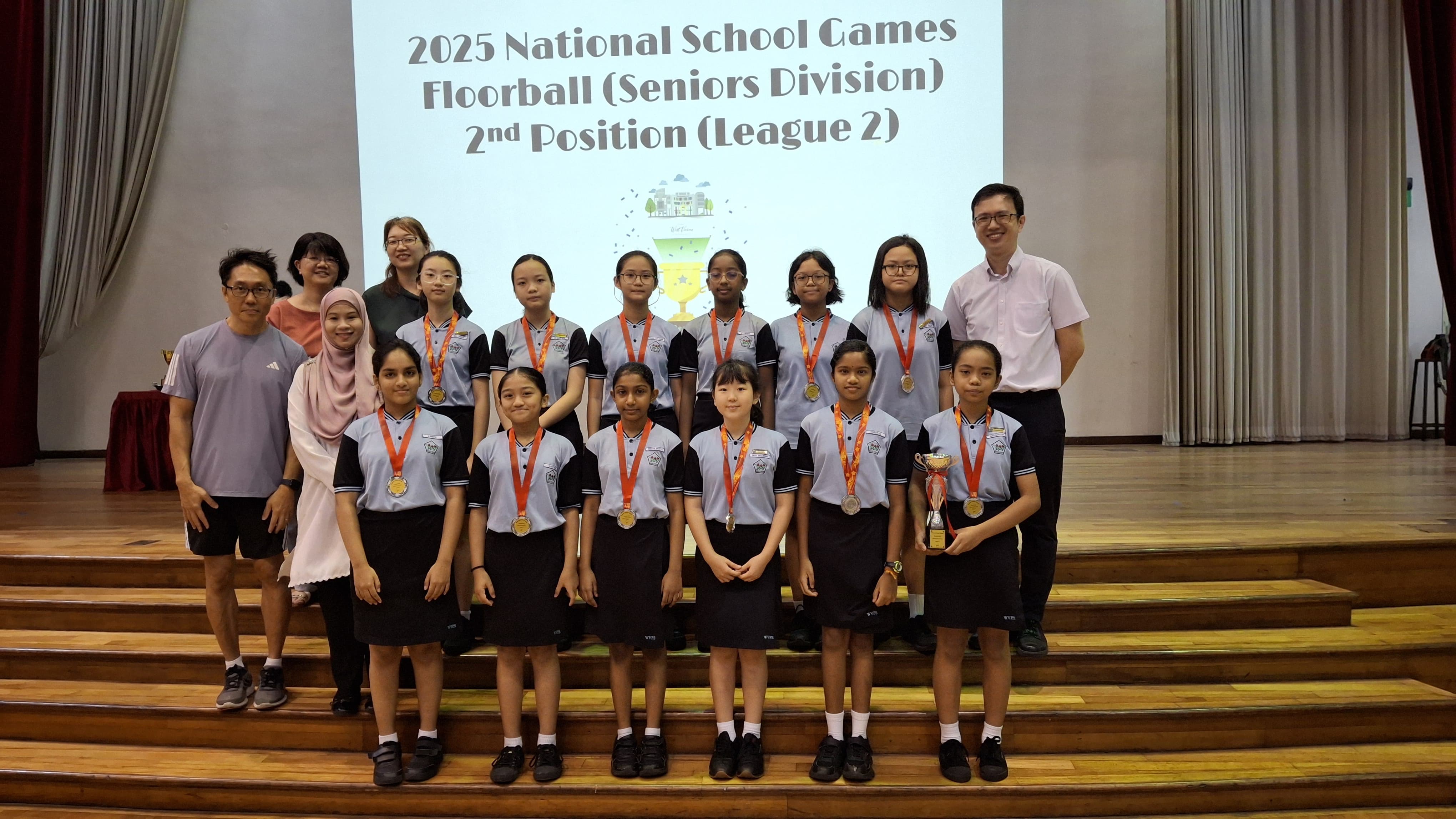 Group of students with medals and a trophy posing on stage before a 2025 National School Games Floorball 2nd Position sign.