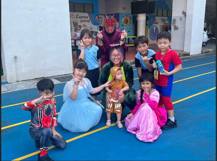 Group of children and adults in costumes including dragon, princess, gingerbread, and Spider-Man posing outdoors.