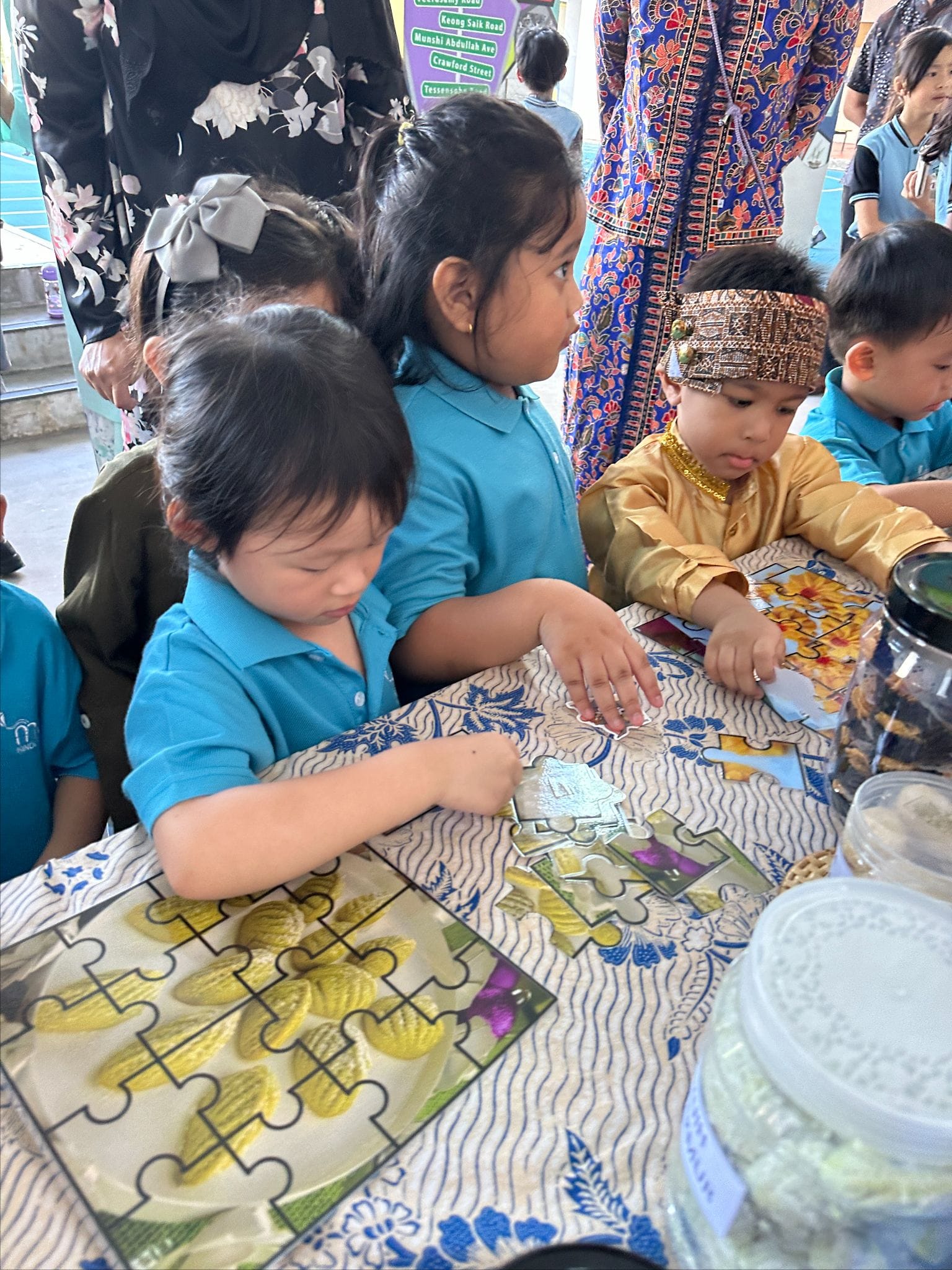 Young children in cultural attire assemble a jigsaw puzzle together at a table with a patterned cloth.