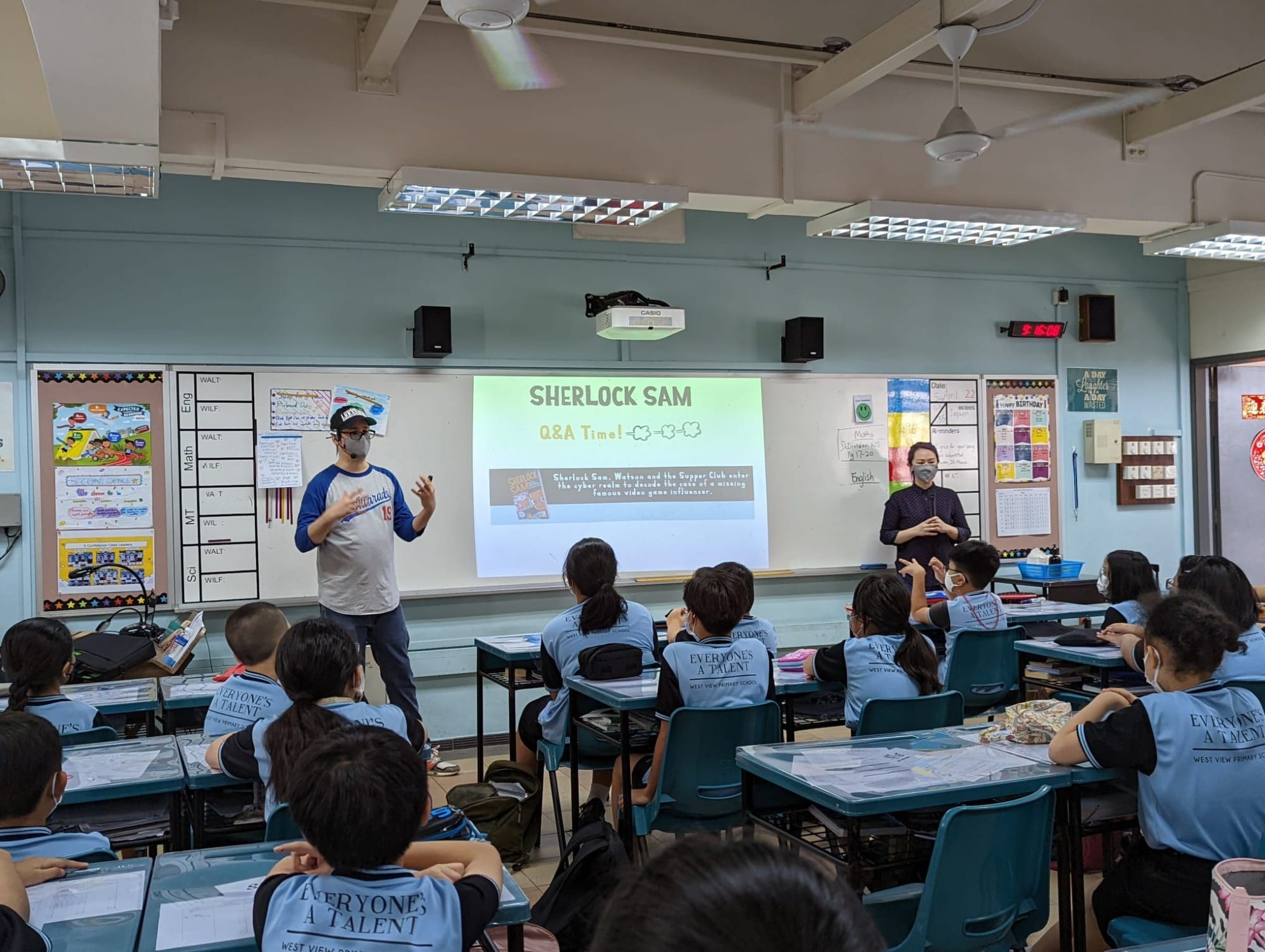 Two presenters stand before a classroom of students with a projected slide reading Sherlock Sam Q&A Time.
