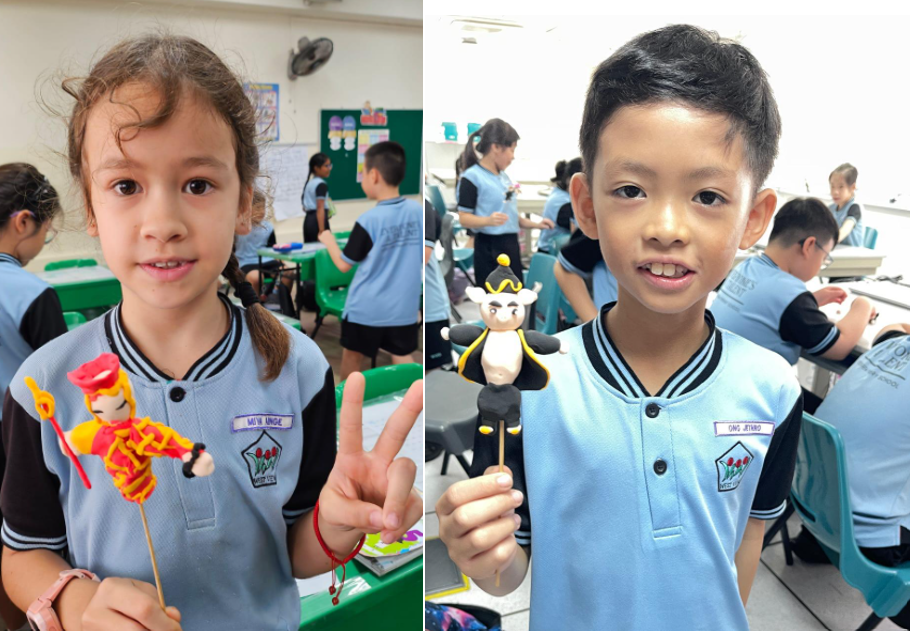 Two young students in blue uniforms hold handmade stick puppets in a classroom setting.