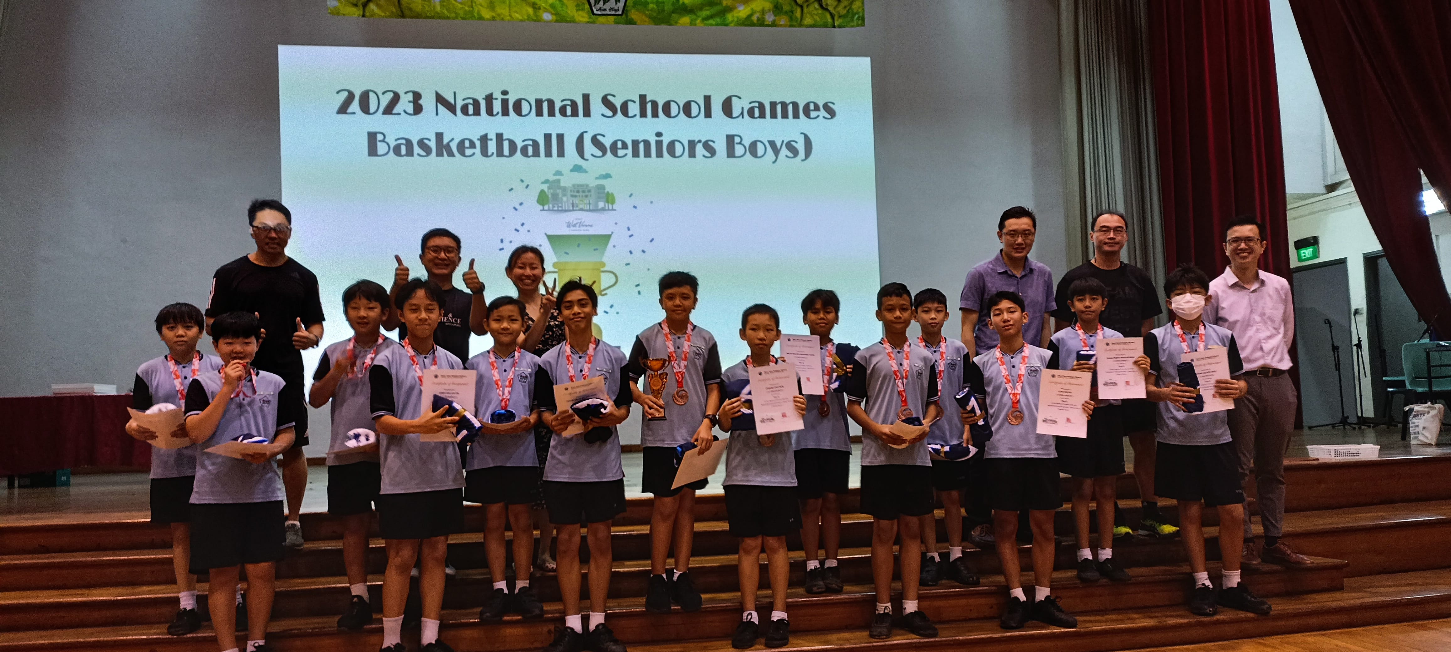 Group of boys in school uniforms holding medals and certificates on stage at 2023 National School Games Basketball Seniors Boys event.
