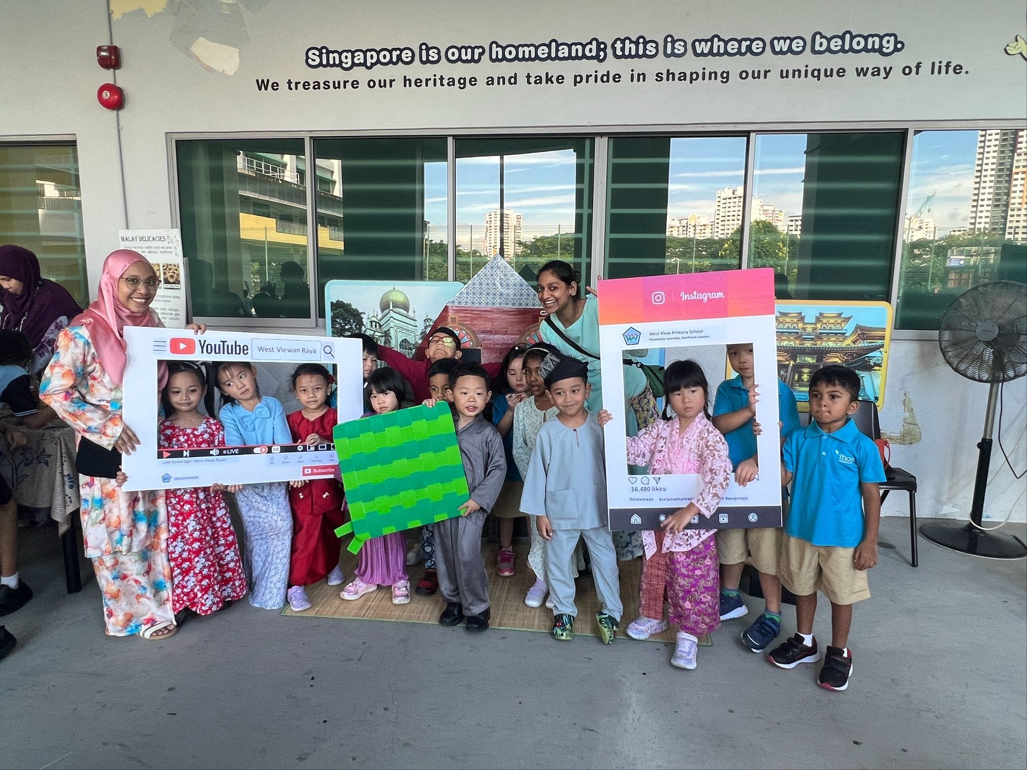 Children and teachers in traditional clothes pose with YouTube and Instagram photo frames at a Singapore school event.