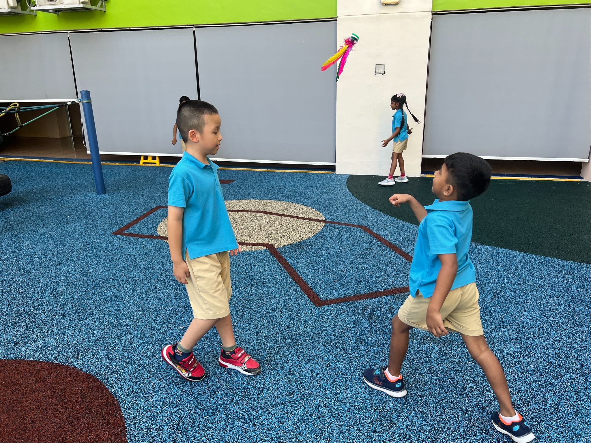 Three children in matching blue uniforms play on a colorful rubber playground floor indoors.