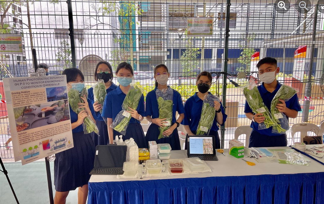 Students holding bundles of leafy greens at a science project display table.