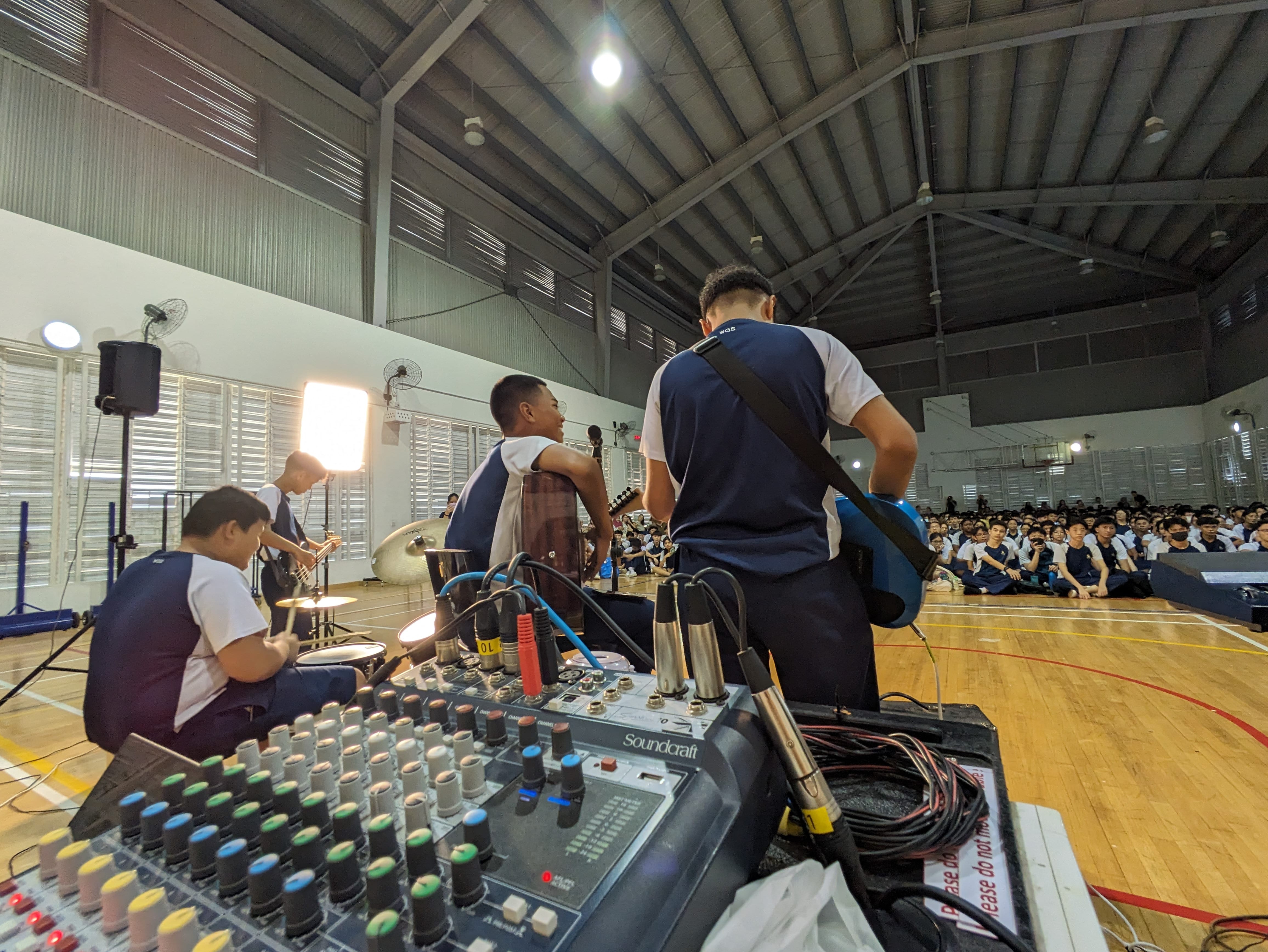 A close up shot of an audio mixer with students performing on stage in front of it.